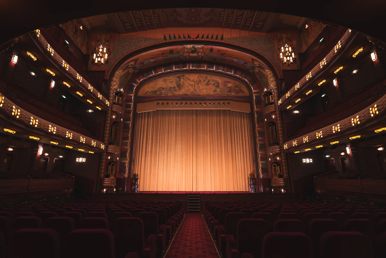 Auditório de teatro com cortina dourada iluminada e plateia vazia
