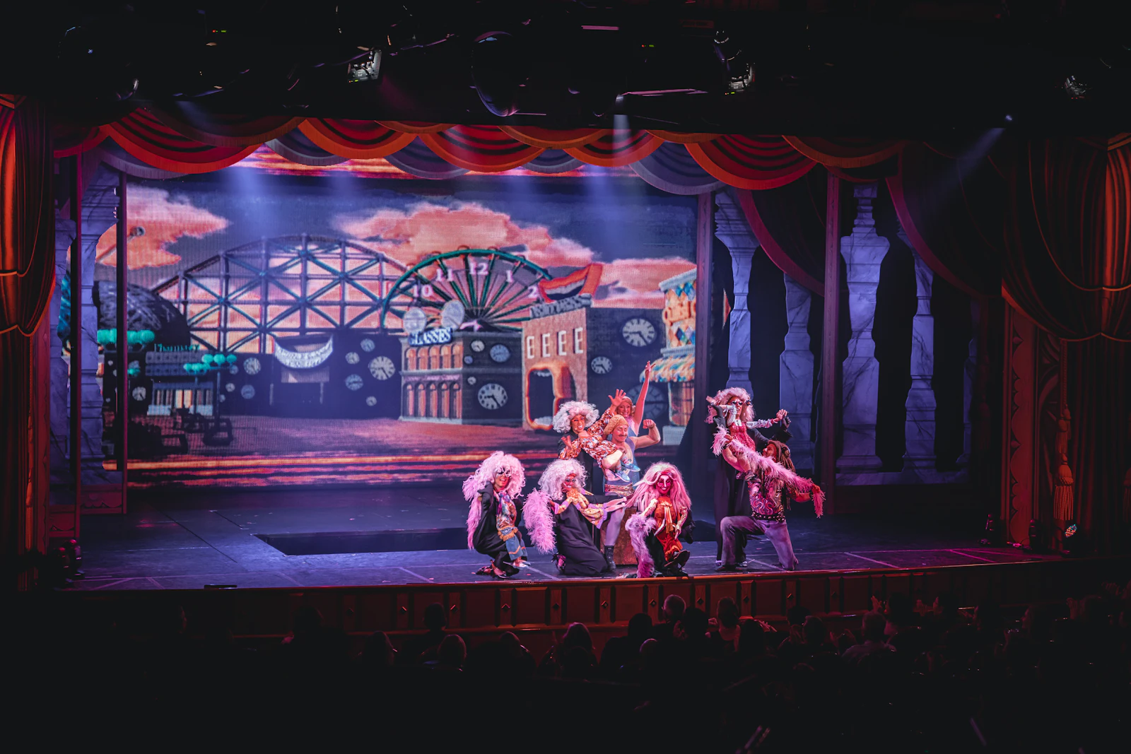 Elenco de um musical em palco com cenário colorido e luzes de cena